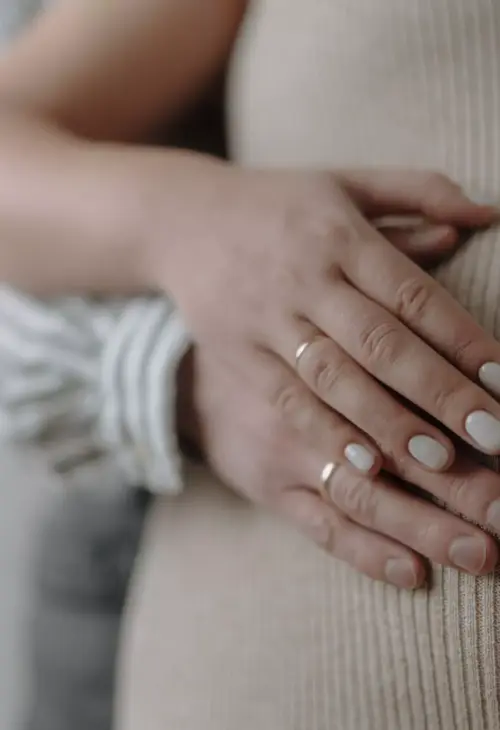 Hände eines Paares liegen liebevoll auf dem Babybauch einer Schwangeren in Nahaufnahme