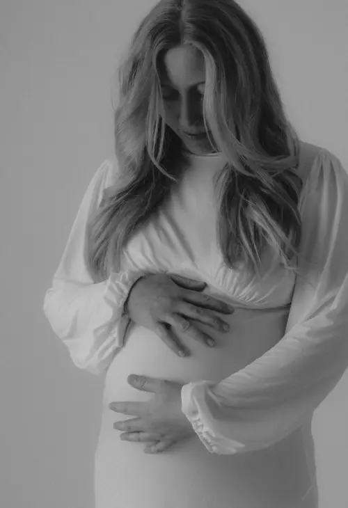 Schwangere Frau im weißen Shirt hält schützend ihren Bauch in ruhigem Licht